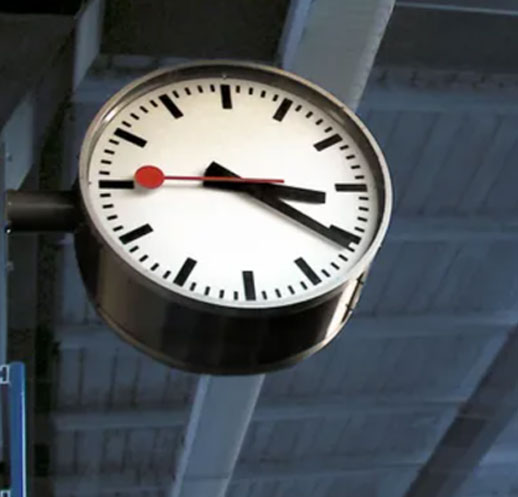 A clock hanging from the ceiling of an office building.